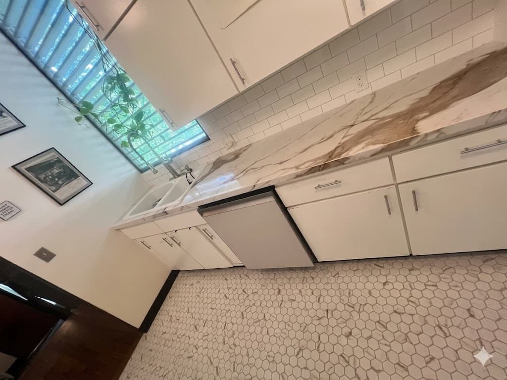 Modern white kitchen featuring marble countertops, subway tile backsplash, and a hexagonal tile floor.