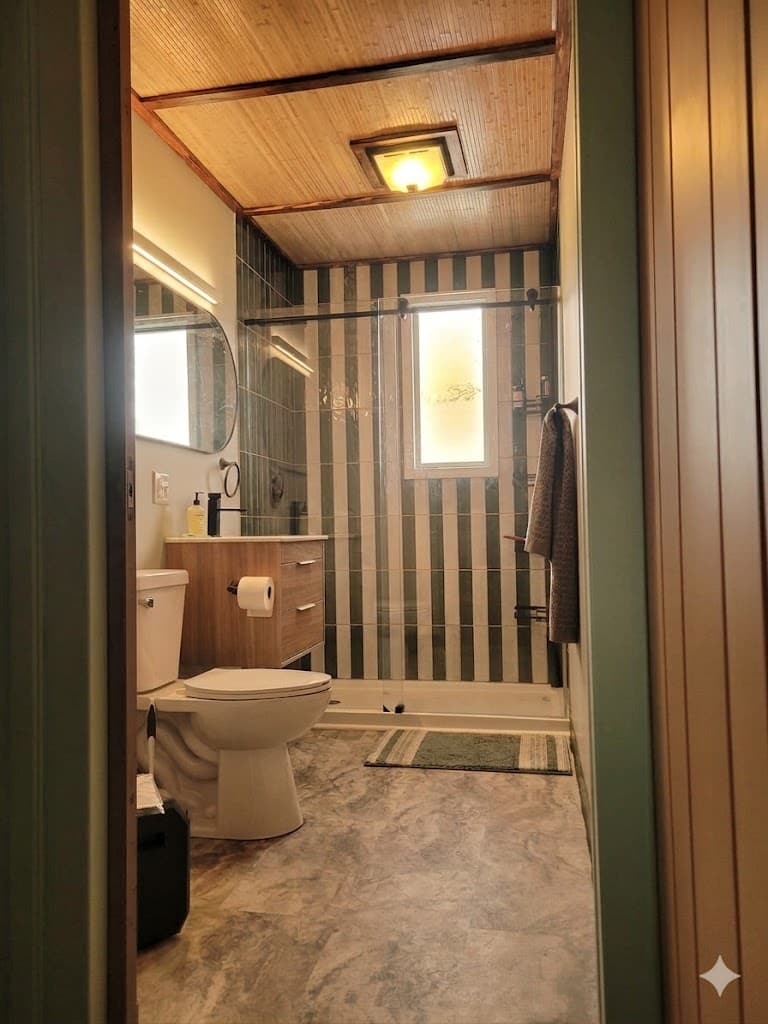 Bathroom with wooden vanity, glass shower with green striped tiles, and bamboo paneled ceiling.