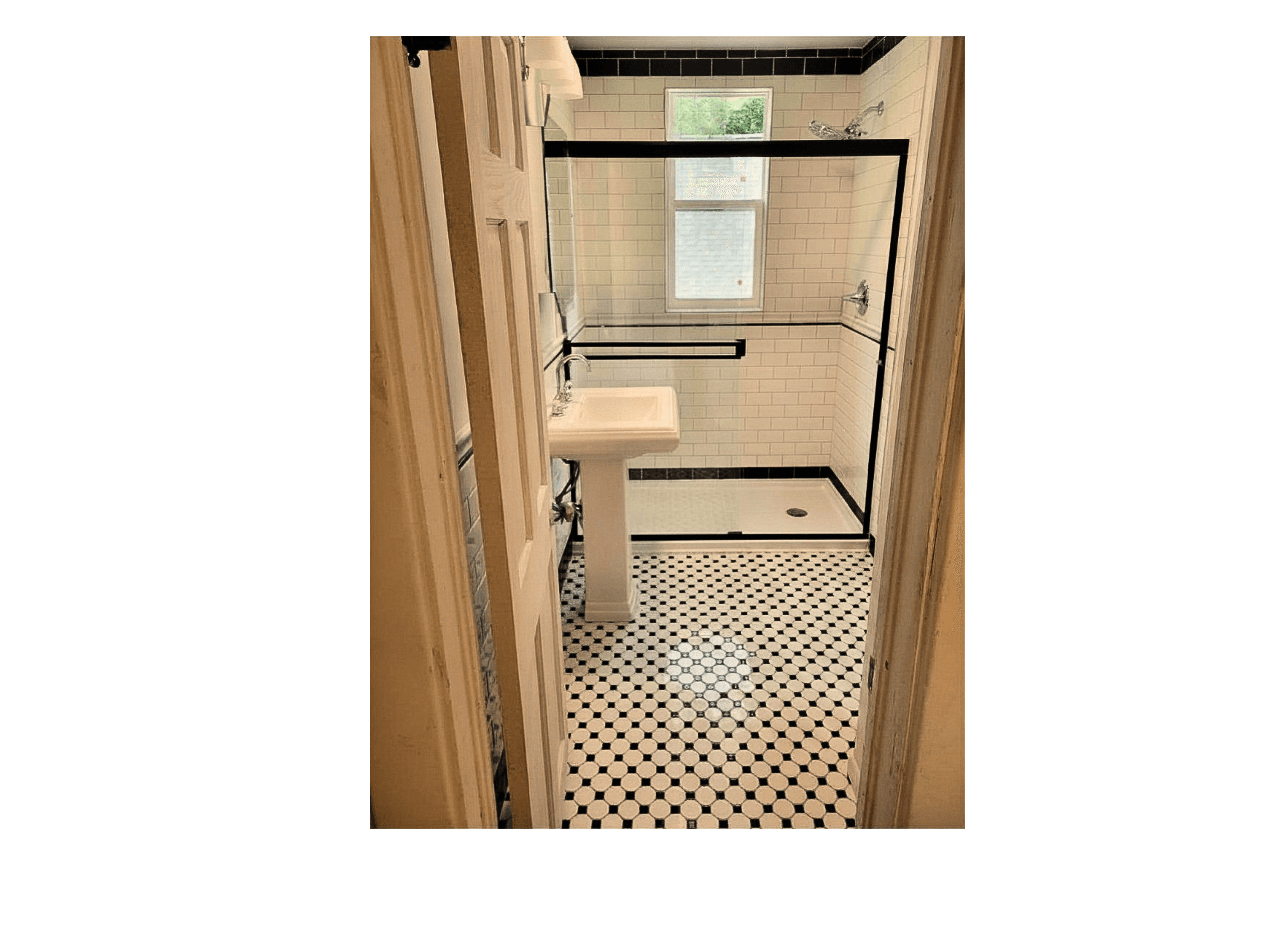 Bathroom with pedestal sink, black and white patterned floor, and glass shower with black trim.