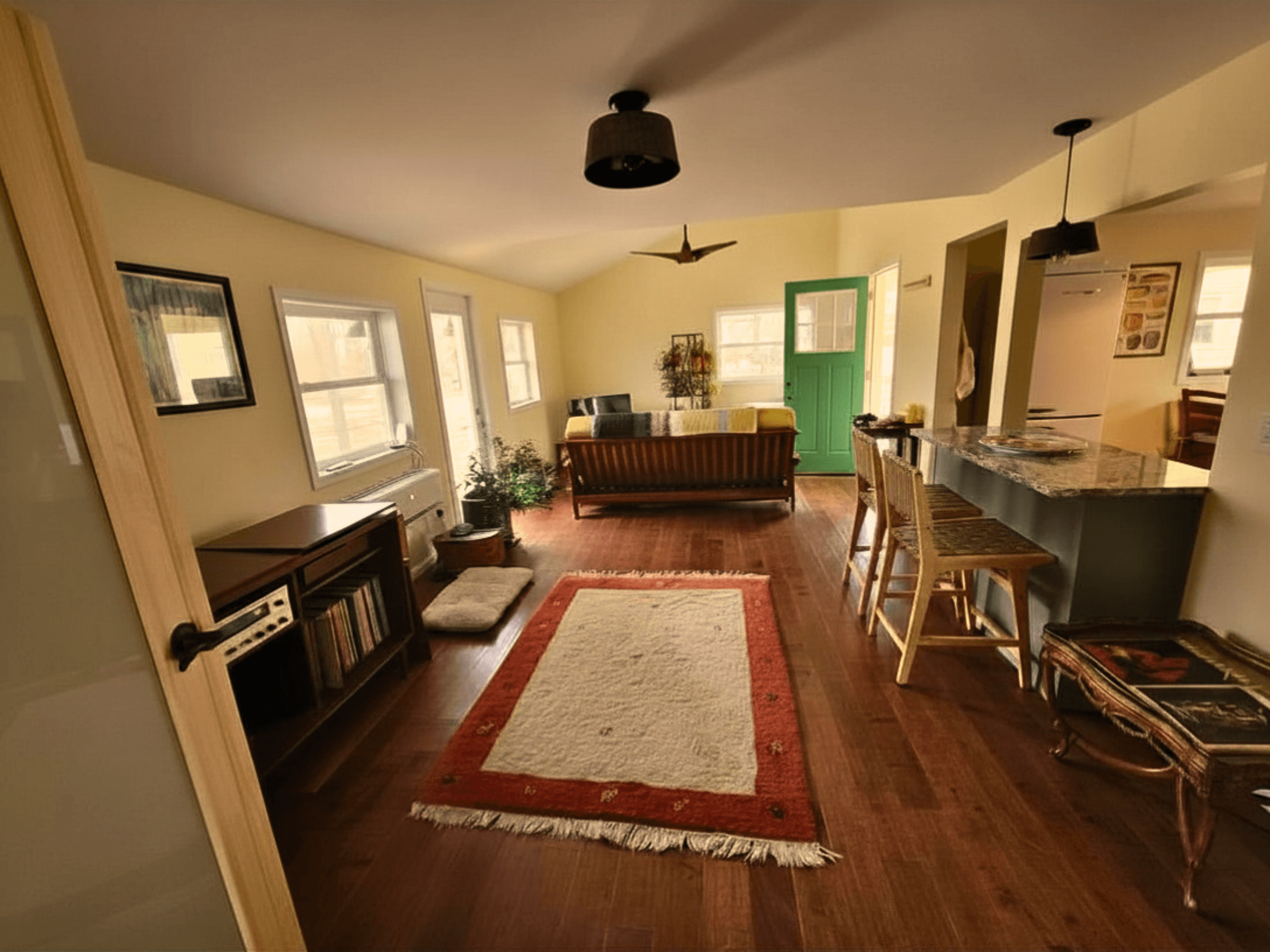 Cozy living area with hardwood floors, a red rug, wooden sofa, and green door.