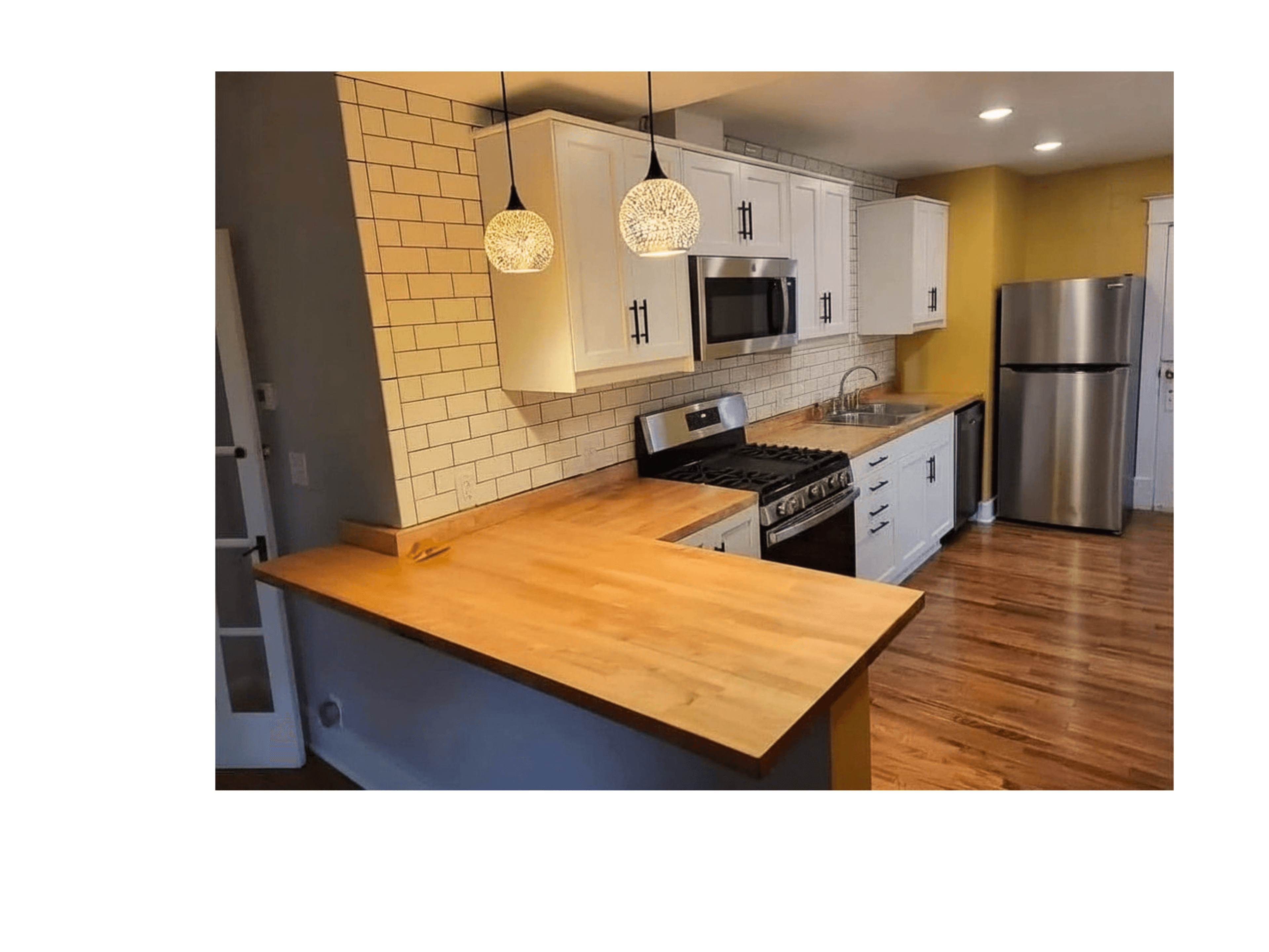 Modern kitchen with white cabinets, butcher block countertops, subway tile backsplash, and stainless steel appliances.