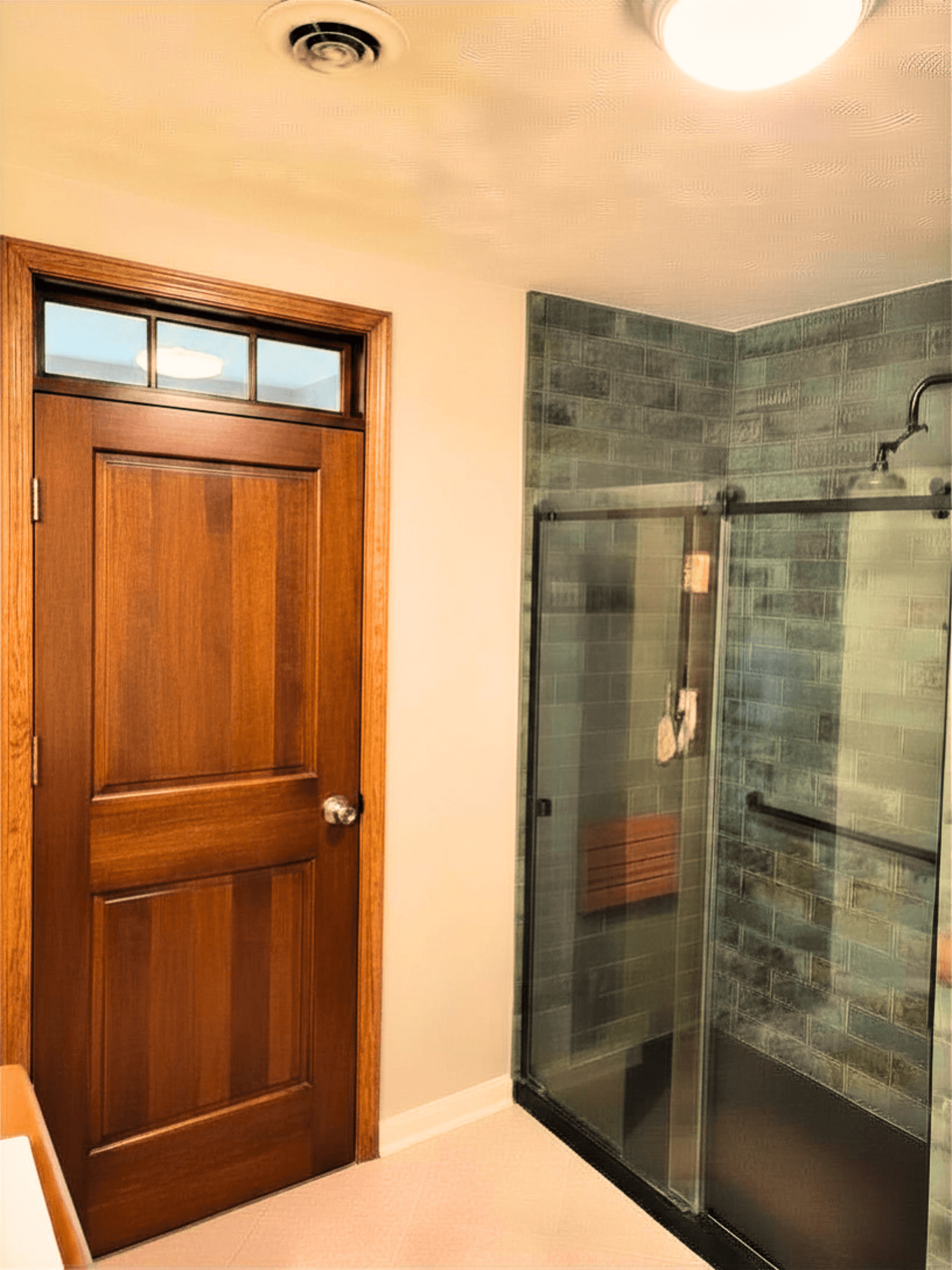 Wooden door with transom window beside a glass shower enclosure with green subway tiles.