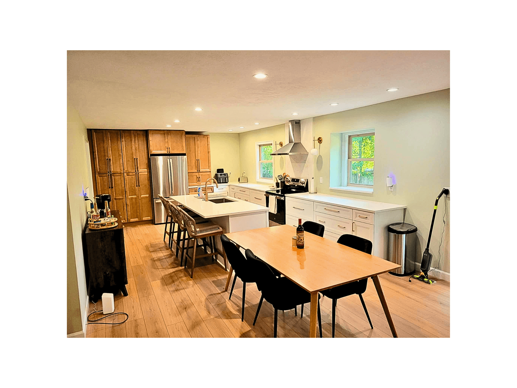 Modern kitchen and dining area featuring light green walls, wooden table, and white island.
