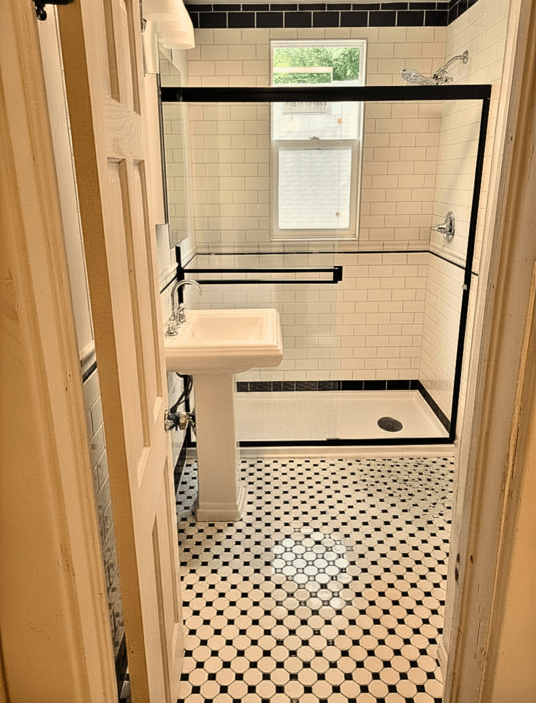 Bathroom with black and white patterned tile floors, a pedestal sink, and subway tile shower.